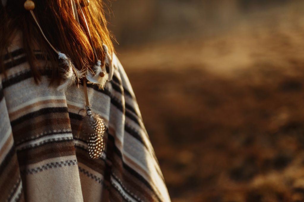 back of native indian american woman walking in mountains in evening, hair with feathers